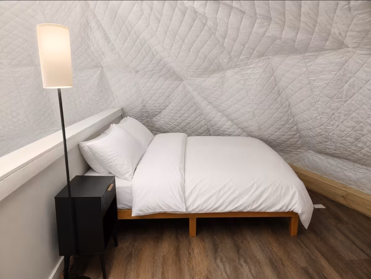 Loft bedroom tucked under the geodesic dome canopy with a queen bed and reading lamp