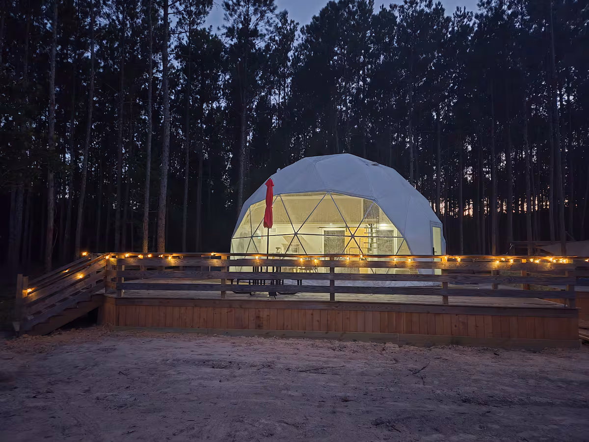Geodesic glamping dome glowing at twilight with string lights along the wooden deck in Kountze, Texas