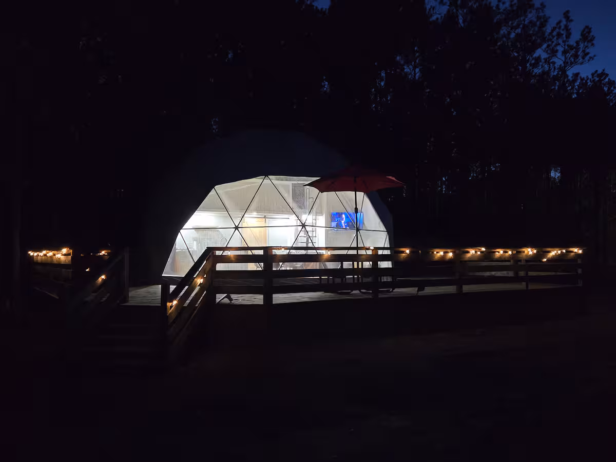 The geodesic dome at The Glamping Spot lit from within at night, surrounded by East Texas pines